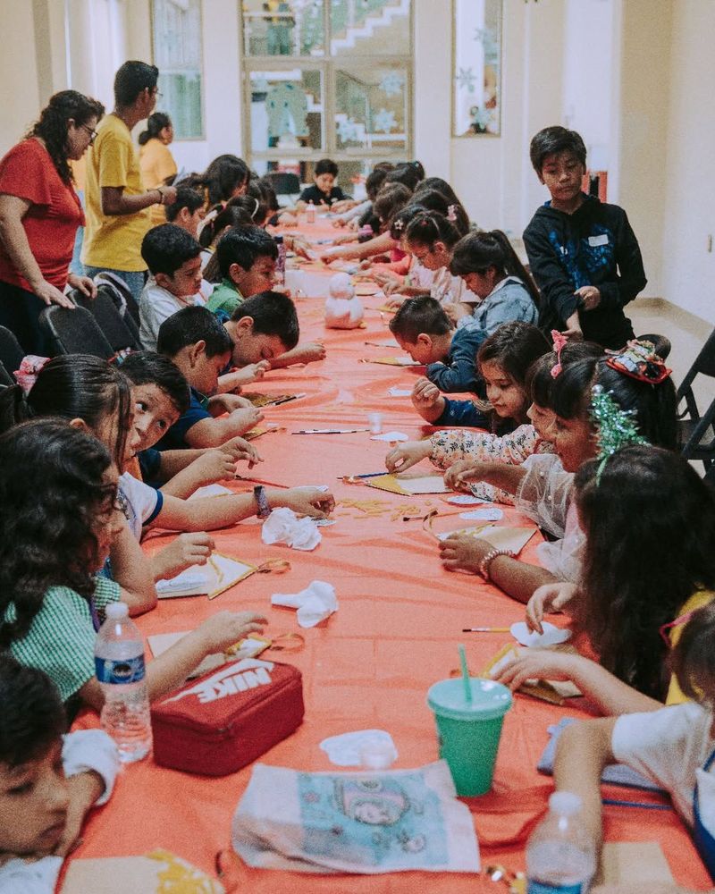 Niños dibujando juntos en una larga mesa durante una actividad.